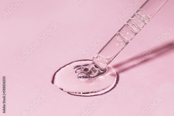 Fototapeta Facial serum with bubbles pouring from glass pipette on light pink background. Transparent liquid gel drop with retinol closeup. Skin care treatment. Trendy beauty cosmetic product macro. Front view.
