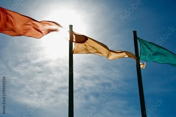 Obraz Three colorful flags flapping in the wind with blue sky and sun Oxnard beach California