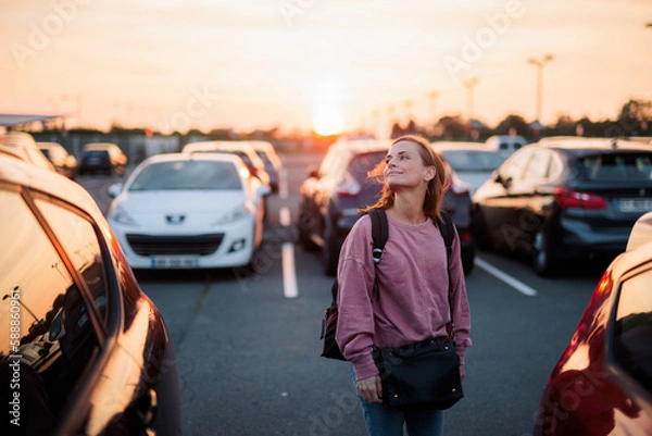 Obraz jeune femme, sur le parking de l'aéroport, heureuse de partir en vacances au coucher du soleil