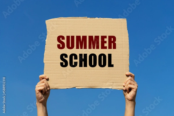 Fototapeta Summer school text on box paper held by 2 hands with isolated blue sky background. This message board can be used as business concept about summer school.