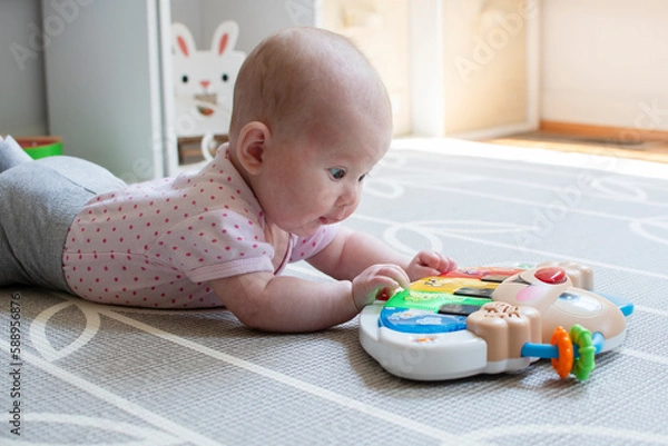 Fototapeta Little Caucasian newborn baby girl playing with a piano toy on the floor during tummy time. Tummy time concept. Baby development. 