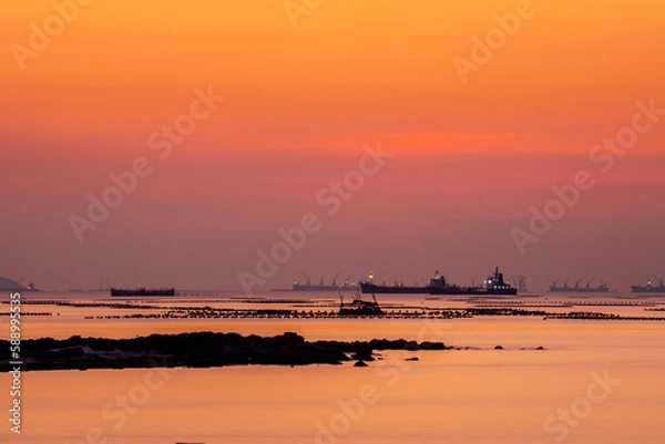 Fototapeta long exposure technic therefore motion blurred effect Smoky and soft sea water surface with small island named Koh Loy boat  rock and commercial vessel container cargo at horizon during sun set