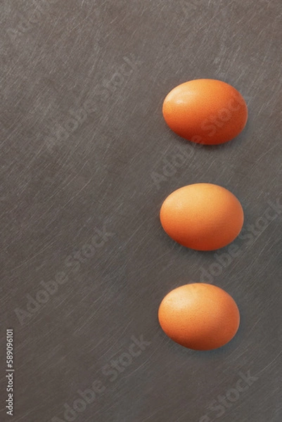 Fototapeta Three color eggs alined on vertical above aluminum surface