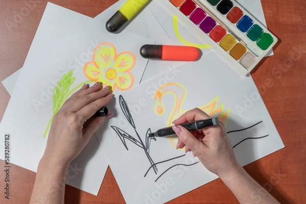 Obraz Women's manicured hands draw with felt-tip pens on a white sheet. At the desk. Top view
