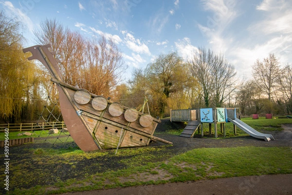 Fototapeta Wooden boat climbing frame structure in outdoor natural public playground with slide in background.