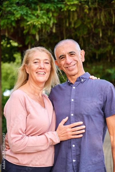 Fototapeta Happy mature couple smiling and looking at camera in a park at street.