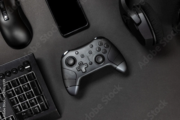 Fototapeta Top view of game controller with gadgets and mobile phone on black gamer desk