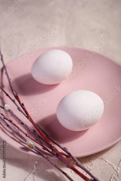Fototapeta Easter table setting with pink plate, willow branches and two white eggs on white table.