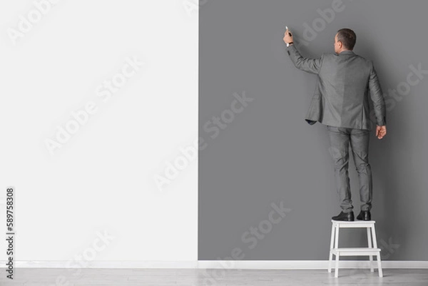 Fototapeta Mature business consultant with marker on stepladder near black and white wall, back view