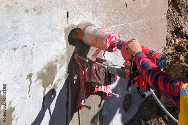 Obraz Worker is drilling to concrete wall with core drill machine. core drill is a drill specifically designed to remove a cylinder of material, much like a hole saw. The material left inside the drill bit.