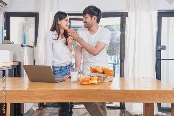 Fototapeta Young Asian couple cooking with fruits and vegetables and using laptop in the kitchen To cook food together within the family happily, family concept.