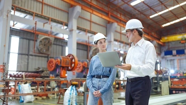 Obraz Two professional engineer man and woman manager leader wearing helmet and holding laptop walking in factory talking and discussing for work