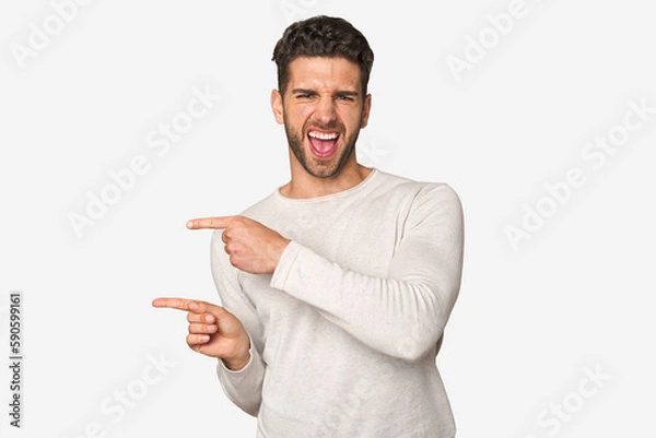 Fototapeta Young handsome man isolated pointing with forefingers to a copy space, expressing excitement and desire.