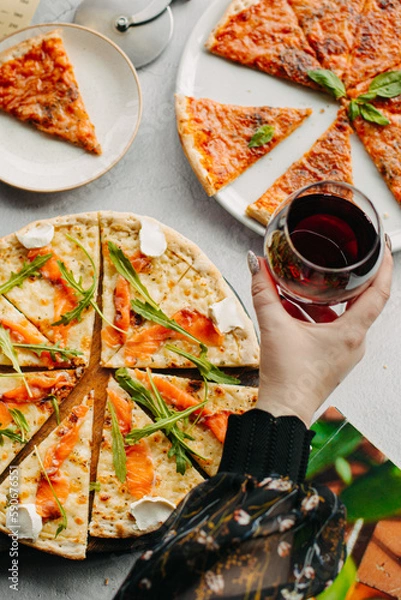 Fototapeta Traditional Italian pizza, vegetables, ingredients on a light background.Top view. a piece of pizza in the hand.Festive table. company of friends