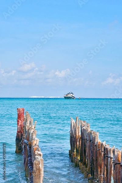Obraz large yacht on the caribbean beaches of cancun Mexico. blue sky with lots of clouds and old wood in foreground out of focus.