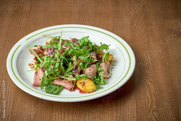 Fototapeta Salad with roast beef, arugula, caramelized onions in a plate on a wooden background