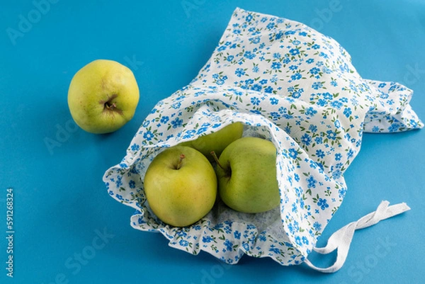 Fototapeta Apples in an eco-bag on a blue background. The concept of reuse, an eco-friendly approach to everyday life.