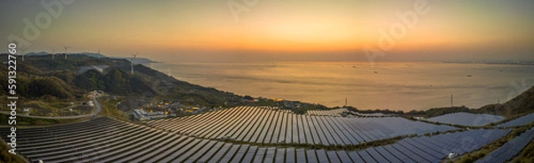 Fototapeta Panoramic view of solar panels and turbines on coastal energy farm at sunset