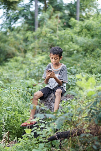 Fototapeta A boy on a tree trunk and looks at his phone