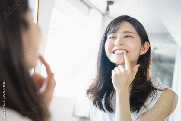 Obraz 鏡で自分の白い歯の状態をチェック確認して笑顔になる30代の若い女性（ビューティーイメージ）