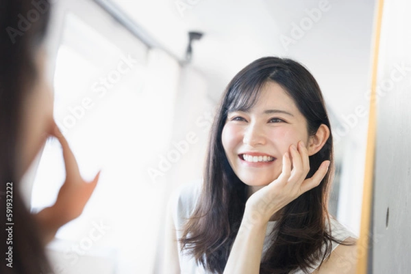 Obraz 姿鏡の前で鏡に映る自分の肌の調子を眺めて笑顔になる20代〜30代の女性