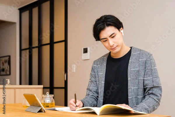 Obraz 自宅のリビングで資格のノートパソコンを広げワイヤレスのイヤフォンをつけ勉強をする30代の社会人の男性