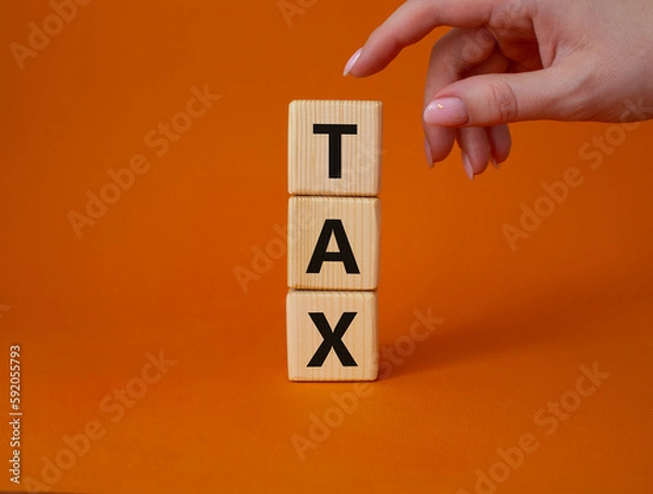 Fototapeta Tax symbol. Wooden cubes with word Tax. Businessman hand. Beautiful orange background. Business and Finace and Tax concept. Copy space.