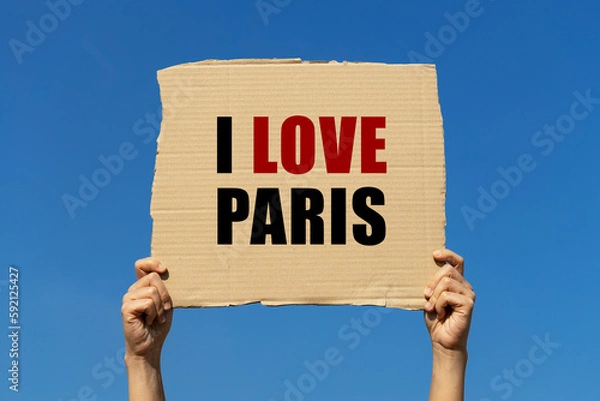 Fototapeta I love Paris text on box paper held by 2 hands with isolated blue sky background. This message board can be used as business concept about loving Paris.