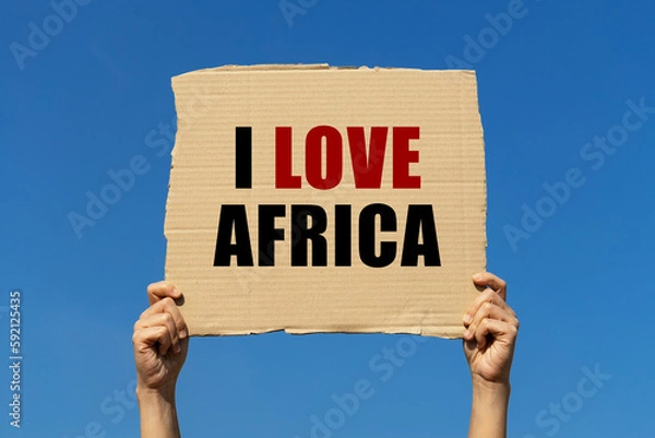 Fototapeta I love Africa text on box paper held by 2 hands with isolated blue sky background. This message board can be used as business concept about loving Africa.