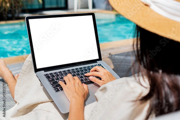 Fototapeta Freelancer using laptop working remotely near swimming pool. Young Asian traveler woman working on computer during her summer holiday. Work from anywhere, Technology and lifestyle concept, copy space