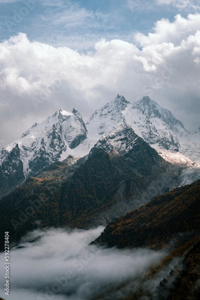 Obraz View of the valley and autumn foggy forest with snow covered mountain peaks