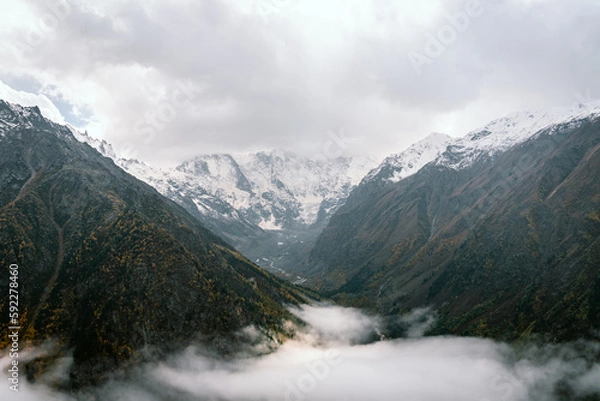 Obraz View of the valley and autumn foggy forest with snow covered mountain peaks