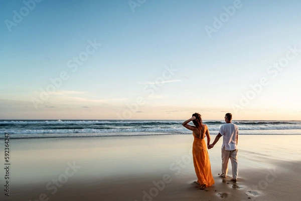Obraz Romantic couple walking on sunset beach, enjoying evening light, relaxing on tropical summer vacation. Honeymoon. Love.