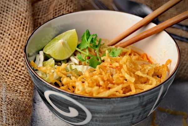 Fototapeta Northern Style Curried Noodle Soup with Chicken, khaao saawy gai, Khao Soi served in a blue cave. on a white table in thailand..