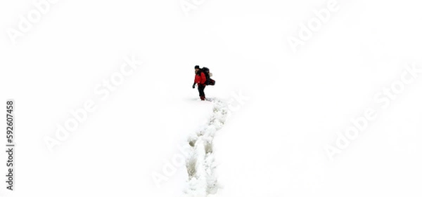 Fototapeta A man in a red jacket with a backpack walking on snow, footprints in snow, behind.