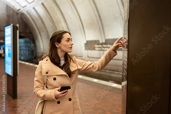 Obraz Washington DC Metro station, a young woman looking at a wall map for directions, holding a cellphone.