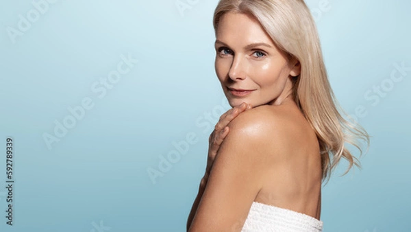 Obraz Mature old lady with beautiful glowing body and face, looks behind her shoulder with confident gaze, has perfect skin, applies anti-aging skincare cream and cosmetic products for nourished face