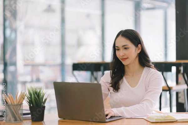 Obraz A portrait of a smiling, young, beautiful, professional, and confident millennial Asian businesswoman using a digital tablet to analyze sales data at a co-working space.