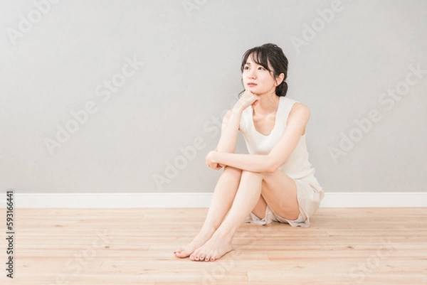 Obraz フローリングに座って頬杖をついて考える・悩む女性（美容・スキンケア・ダイエット）
