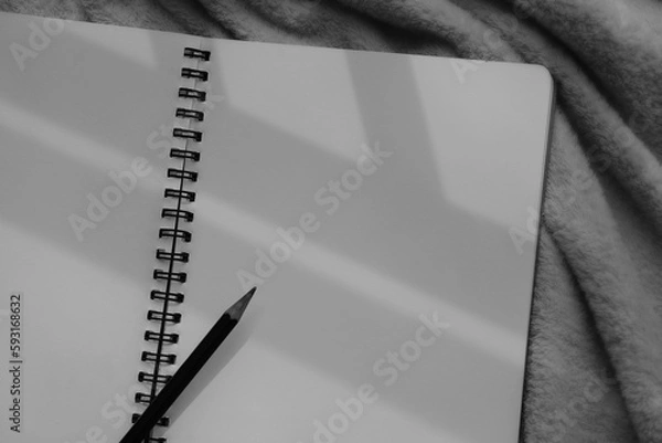 Fototapeta Monochrome image of notebook and pencil against sunlight and beautiful shadows with space for text. Selective focus.
