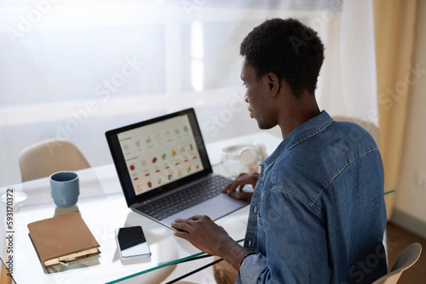 Fototapeta High angle view at black young man using online shopping website for grocery delivery, copy space