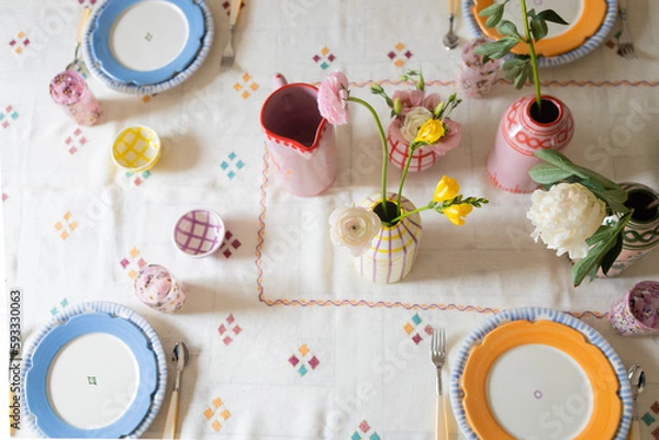 Fototapeta horizontal overhead shot of colorful ceramics and fresh flowers on embroidered tablecloth