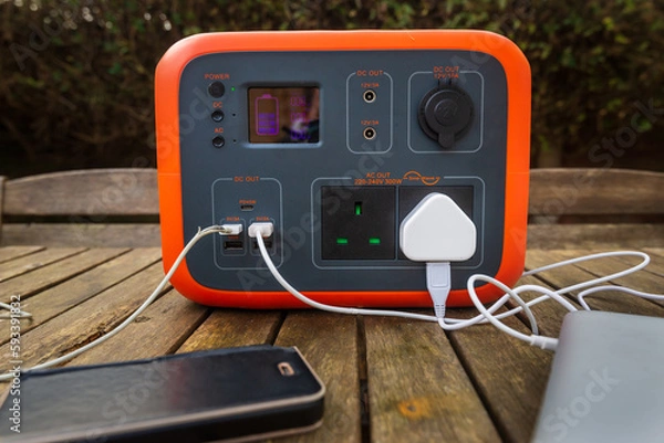 Fototapeta Portable power station solar electricity generator on table with mobile phone and laptop charging.