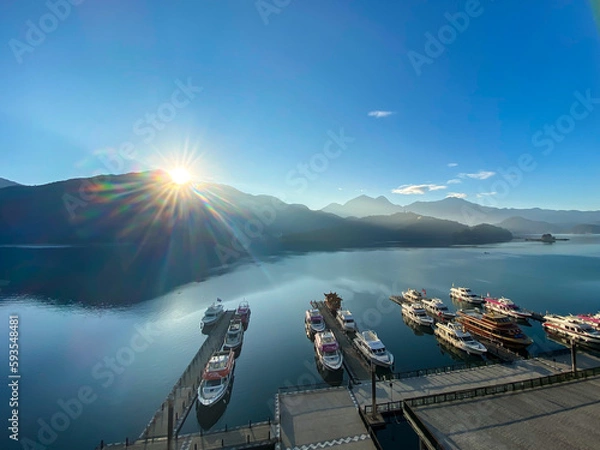 Fototapeta 台湾　日月潭の日の出のサンビーム、山は水面に反映している。埠頭にはしけ船が数台とまっている