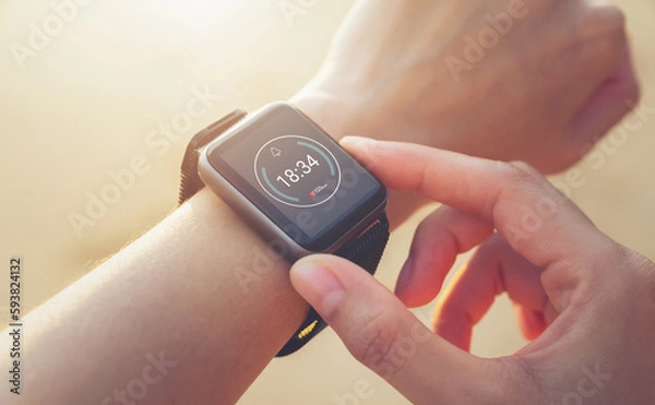 Obraz Woman hand wearing a smartwatch and checking active lifestyle and using fitness tracker outdoor on the beach.