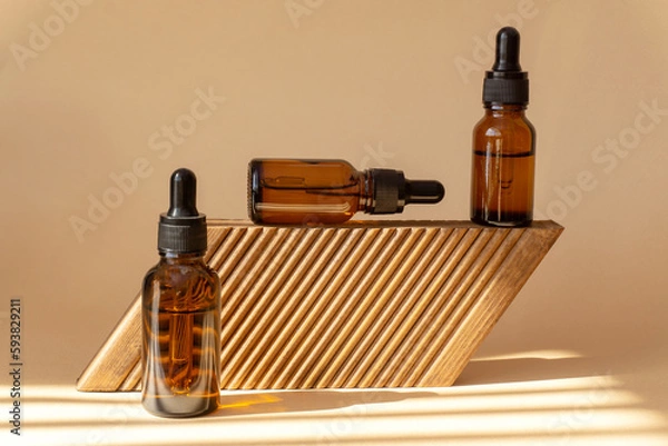 Obraz Bottles with cosmetic serum on wooden platform. Glass vials with a dropper lid in sunlight. Amber cosmetic packaging on a brown background. Conceptual mockup, branding