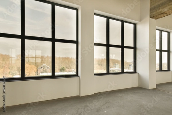 Obraz an empty room with large windows and no one person standing in the window looking out to the city outside,