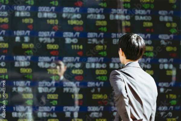 Fototapeta 屋外の株価ボードの電光掲示板を見る30代のビジネスマン投資家男性の後ろ姿