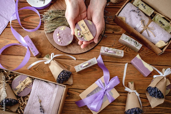 Obraz Fragrant lavender bouquets wrapped in craft paper with ribbon, natural soap and gift boxes on a wooden table. Concept of packing handmade presents