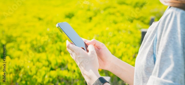 Fototapeta Woman standing on a bridge in the garden and using smartphone in public areas, During leisure time. The concept of using the phone is essential in everyday life.